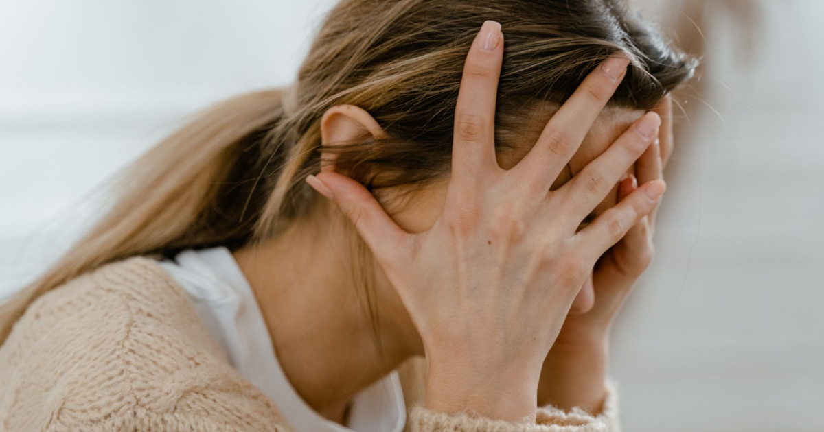 A close up photo of a woman with her head in her hands, stressed from seeing politicians screw up yet again.
